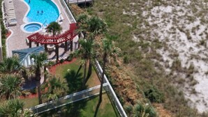 An aerial view of a beach resort with a large swimming pool, beach umbrellas, and a pier extending into the ocean. - Stunning Beach Views of Gulf-14th Floor-Dog friendly-See the longest pier in FL! (Navarre)