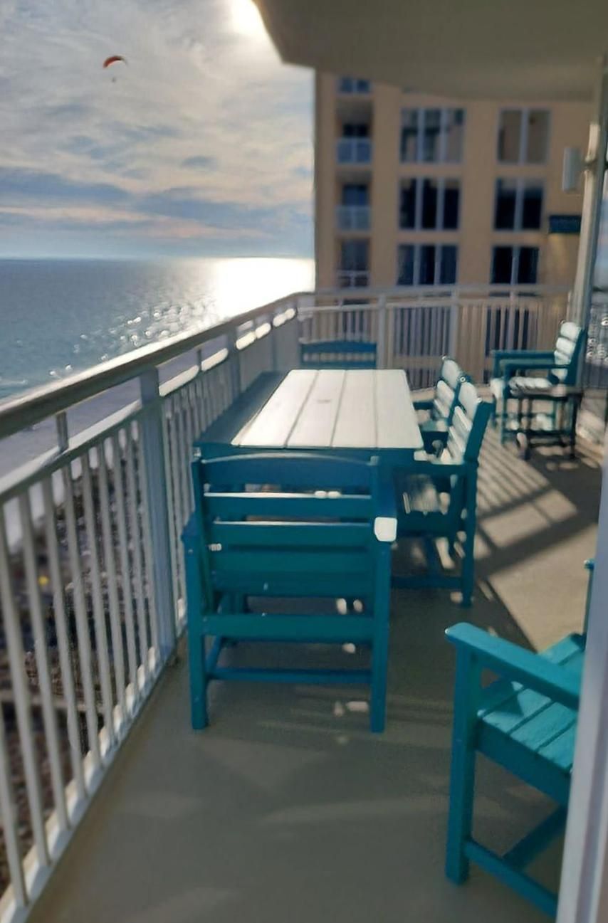 A balcony with a table and chairs, overlooking the ocean.