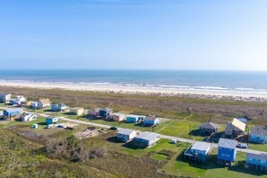 Vue aérienne d’un quartier résidentiel situé sur la côte, avec des maisons et une plage en arrière-plan.