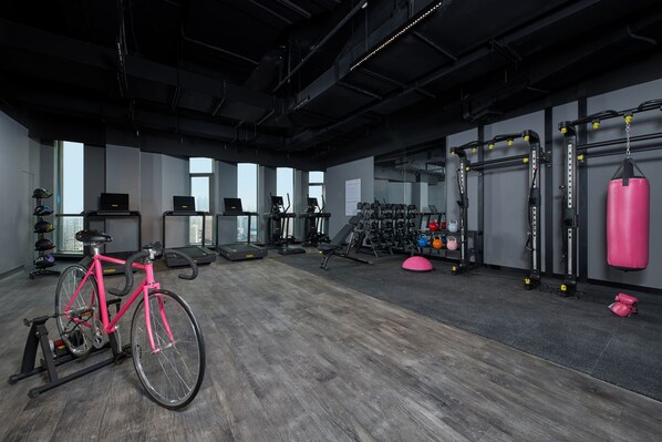 Un gimnasio con una bicicleta estática, cintas de correr, máquinas de pesas y un saco de boxeo.