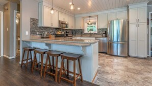A modern kitchen with a central island, bar stools, stainless steel appliances, and a stone backsplash. - Lakefront Retreat with Game Room, Hot Tub, and Gym! (Goodview)