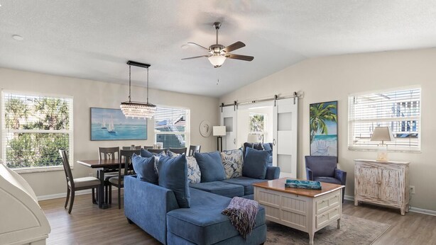 A spacious living room with a blue sectional sofa, a dining area with a table and chairs, and a ceiling fan.