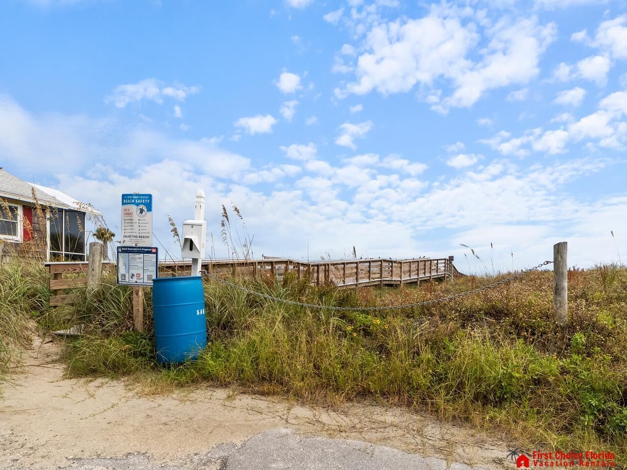A beach area with a wooden boardwalk, a blue barrel, and safety signs.