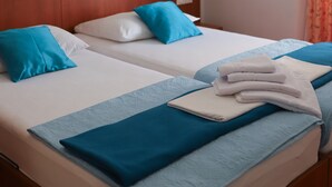 A hotel room with two beds, each with blue and white bedding, a wooden headboard, a framed picture on the wall, and a window with orange curtains.