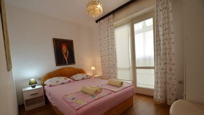 Une chambre à coucher avec un lit, des tables de chevet, une lampe, une fenêtre avec des rideaux et un tableau au mur.