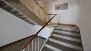 Un escalier avec une rampe en bois et des balustres blanches, menant à un palier sur lequel est fixé un luminaire.