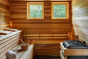 A sauna with wooden walls, two windows, benches, a massage table, and a bucket with a brush.