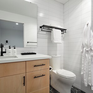 A modern bathroom with a white sink, mirror, and toilet. There are two bottles of hand soap and a glass on the sink. A towel rack is mounted on the wall above the toilet.