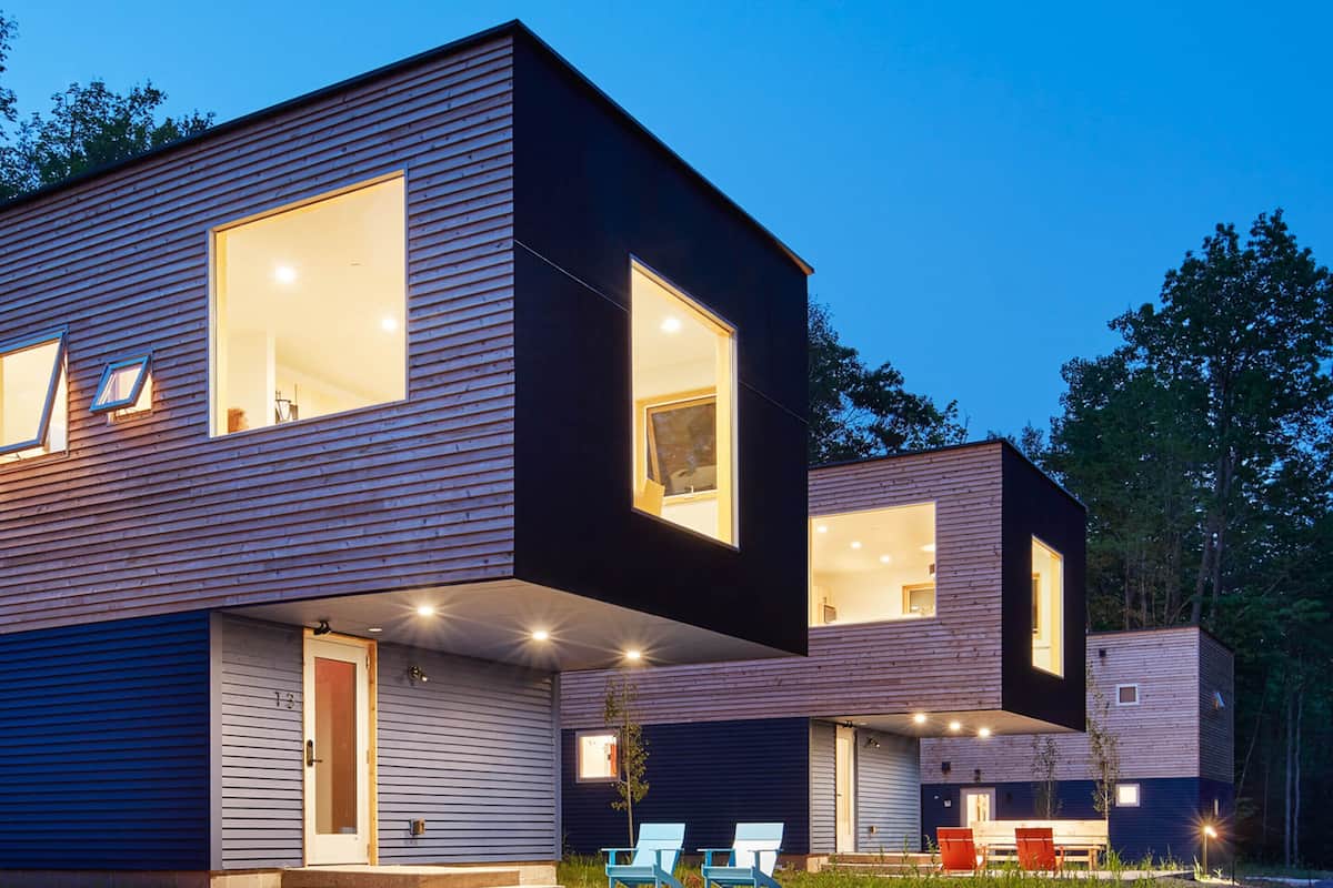 A modern two-story house with large windows, a flat roof, and a well-lit exterior.