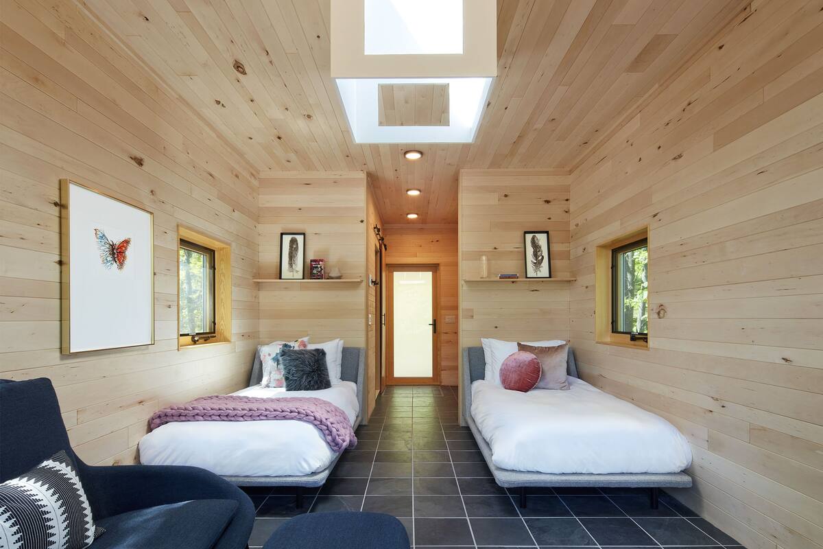 A wooden cabin with two beds, a skylight, and a hallway leading to a door.