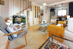 Ein modernes Wohnzimmer mit Fernseher, Sitzgelegenheiten und einer Treppe.