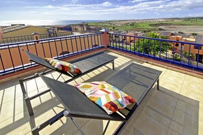 Ein Balkon mit zwei Liegestühlen und einem farbenfrohen Kissen mit Blick auf eine Küstenlandschaft.