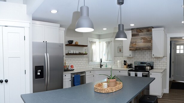 Una cocina moderna con armarios blancos, una isla central, iluminación colgante y un revestimiento de piedra.
