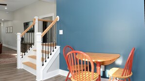 Un comedor con mesa de madera y sillas rojas, una escalera con barandillas blancas y una pared azul decorativa.