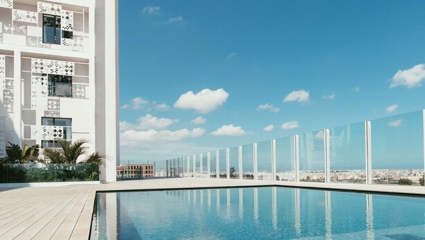 A modern building with a pool area, clear blue sky, and distant cityscape. - Hilton Garden Inn Casablanca Sud (Casablanca)
