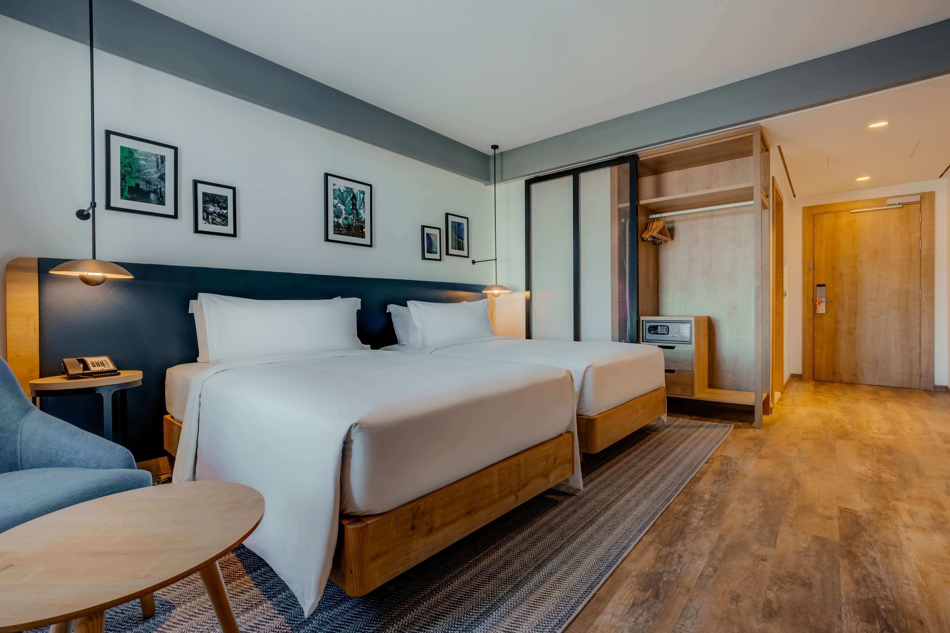 Quarto de hotel moderno com duas camas, uma escrivaninha, uma cadeira e um guarda-roupa.