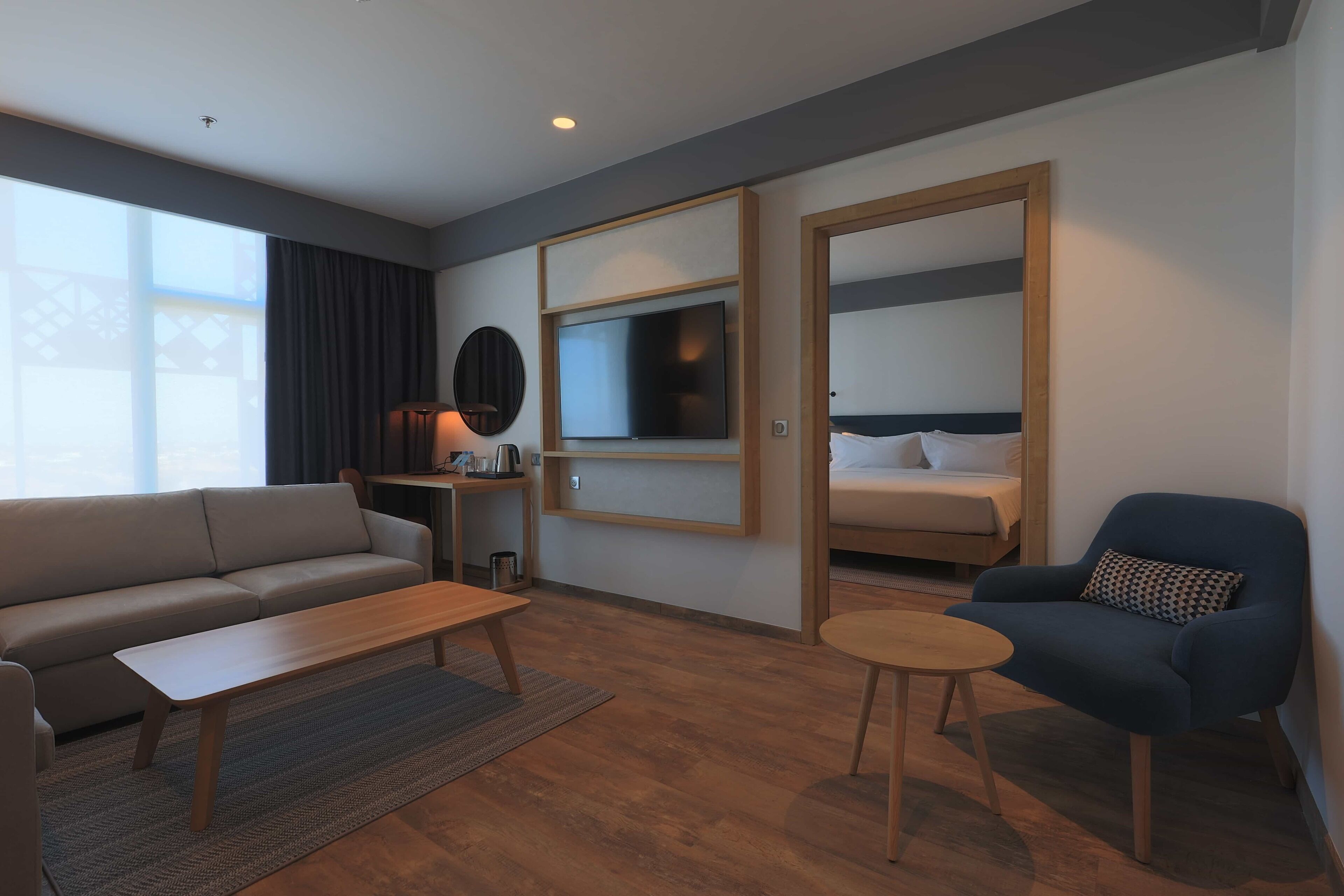 Ein modernes Hotelzimmer mit einer Couch, einem kleinen Tisch, einem blauen Sessel, einem Bett, einem Fernseher und einem Schreibtisch mit einer Lampe.