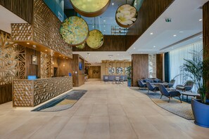 Un moderno vestíbulo de hotel con mostrador de recepción, zona de estar y arreglos florales decorativos.