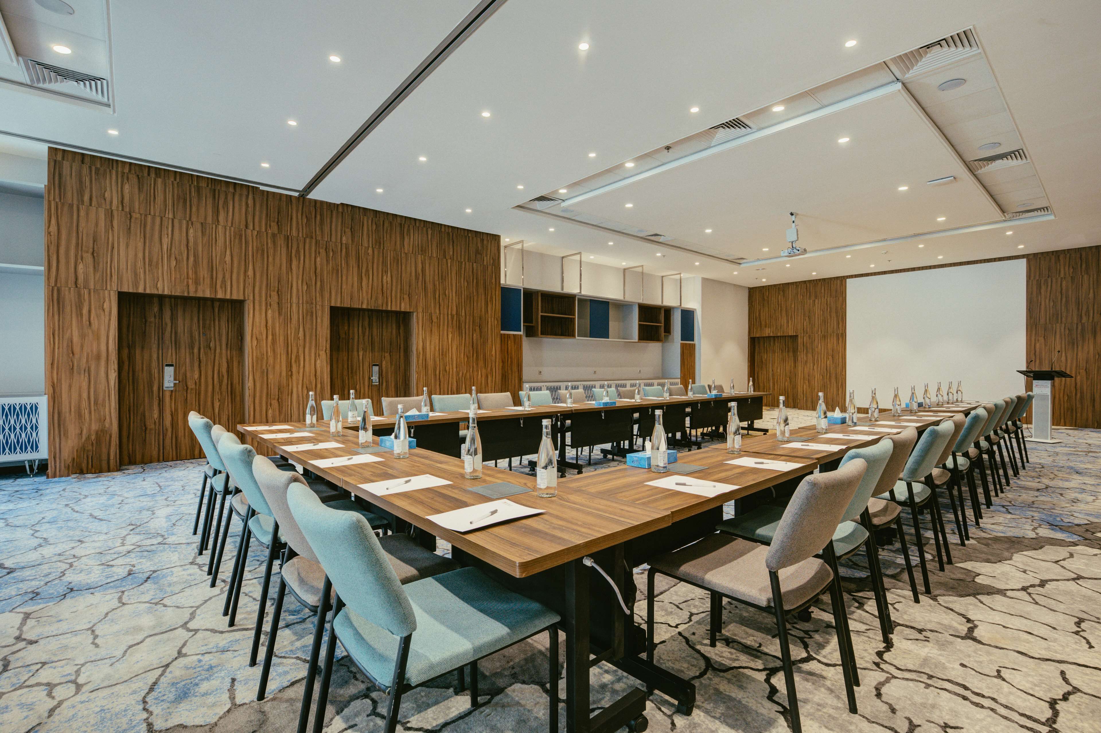 Un salón de conferencias con una larga mesa, sillas y una pantalla de proyector.