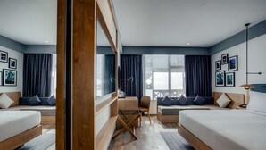 A modern hotel room with two beds, a sofa, a small table, and a chair. There are large windows with curtains, and artwork on the walls. - Hilton Garden Inn Casablanca Sud (Casablanca)