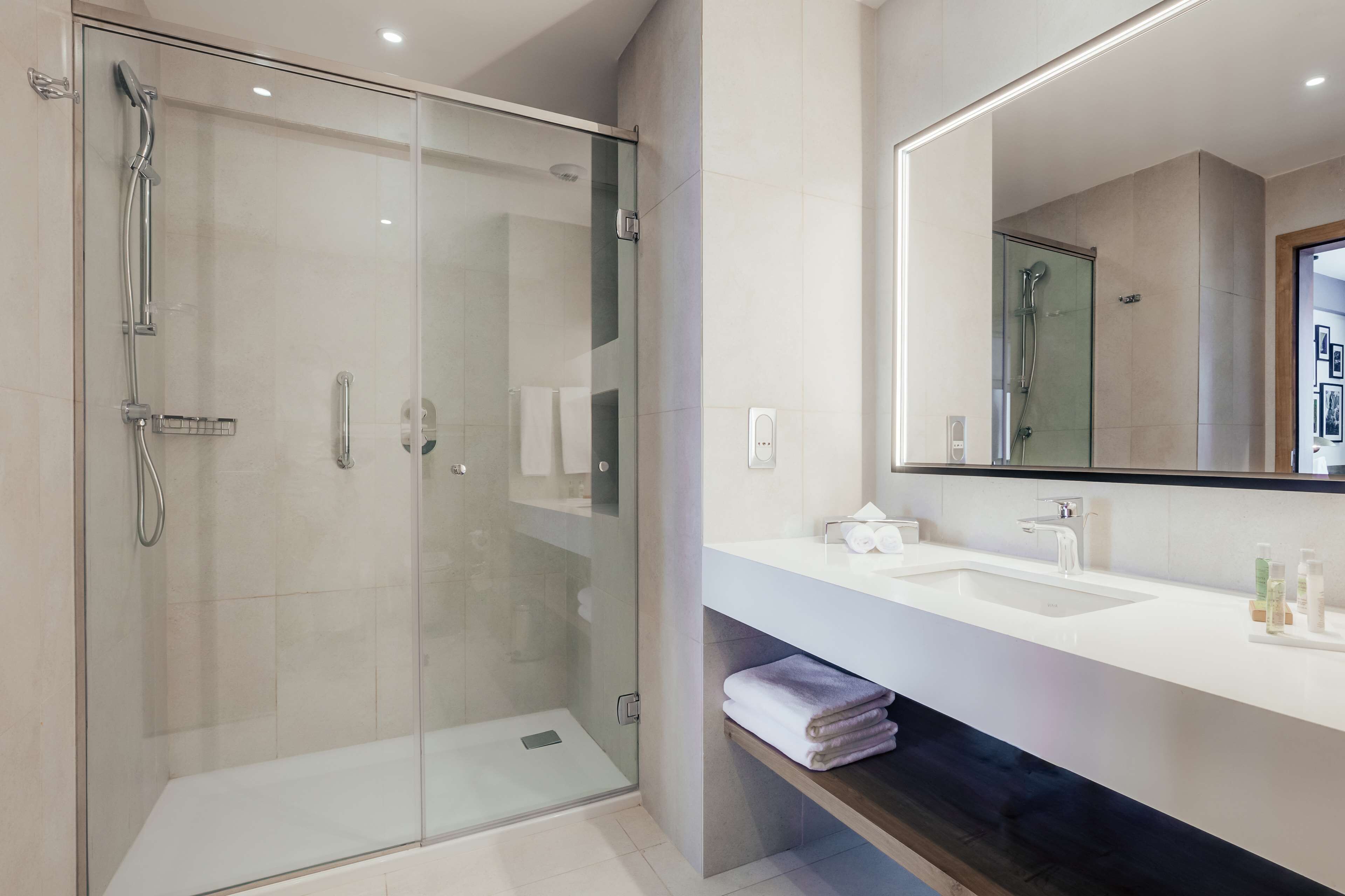 Une salle de bain moderne avec une douche à parois de verre, un grand miroir et un lavabo blanc avec un meuble-vasque.