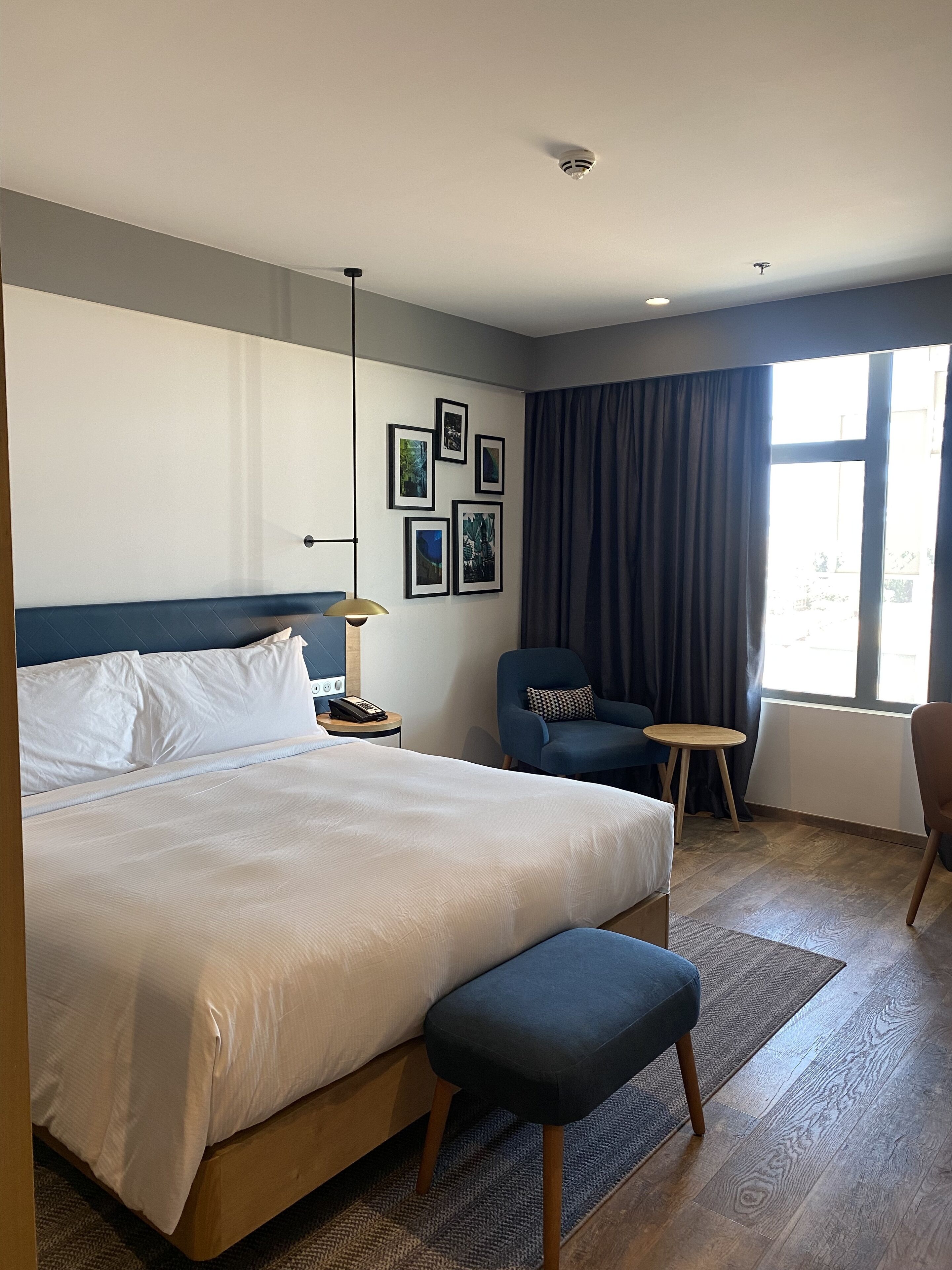 A hotel room with a large bed, a chair, a small table, and a window with curtains.