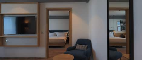 A modern hotel room with a flat-screen TV, a bed, a blue armchair, and a small wooden table.