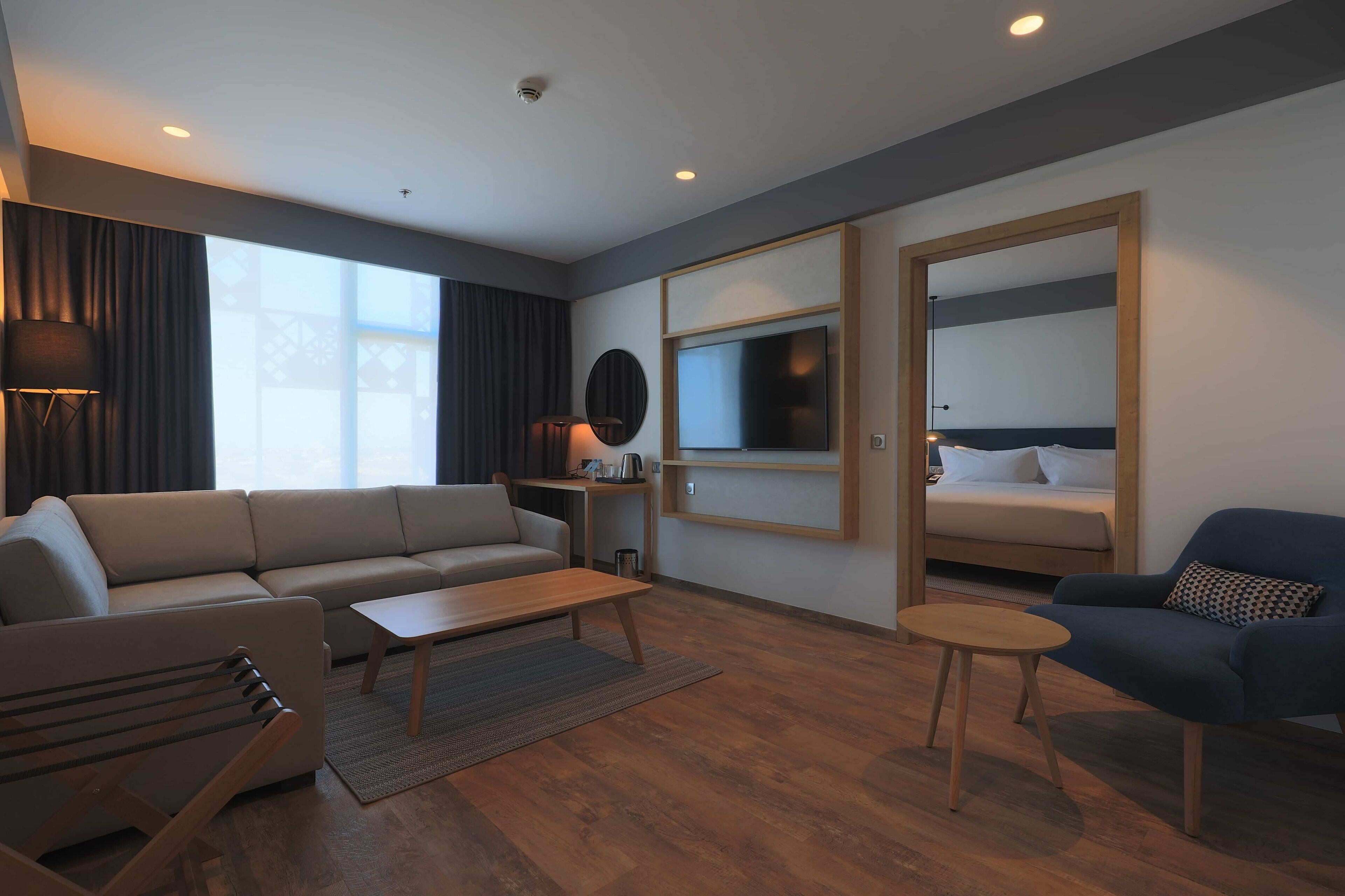 Et moderne hotelværelse med sofa, lænestol, sofabord, fjernsyn og en seng med sengegavl.