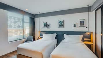 A hotel room with two beds, a large window with a view, and several framed pictures on the wall.