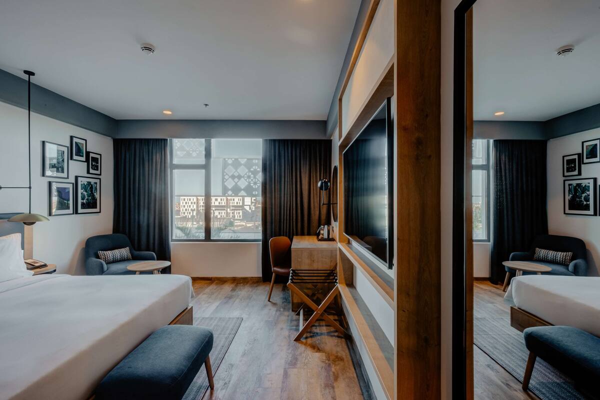 A hotel room with a large bed, a desk, a chair, and a TV.