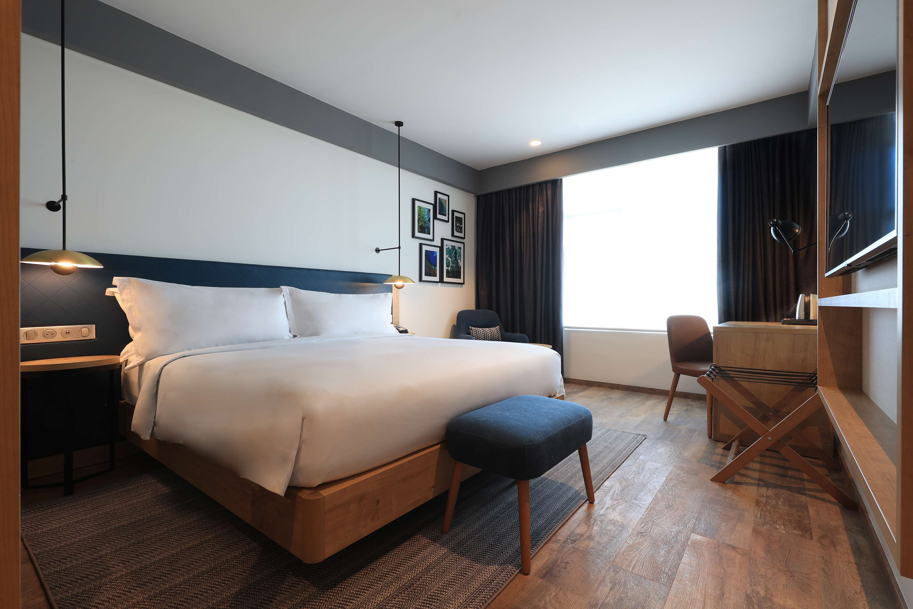 Ein modernes Hotelzimmer mit einem großen Bett, einem Schreibtisch, einem Sessel und einem Spiegel.