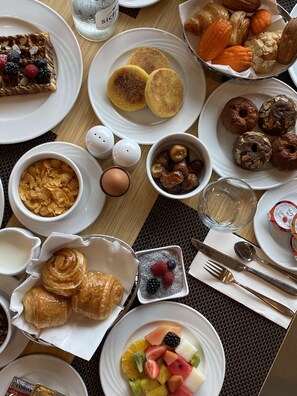 Una mesa de desayuno con diversos platos, como panqueques, pastelería y fruta.