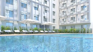 Zona de piscina moderna con tumbonas y sombrillas, rodeada de exuberante vegetación y un edificio con ventanas decorativas.