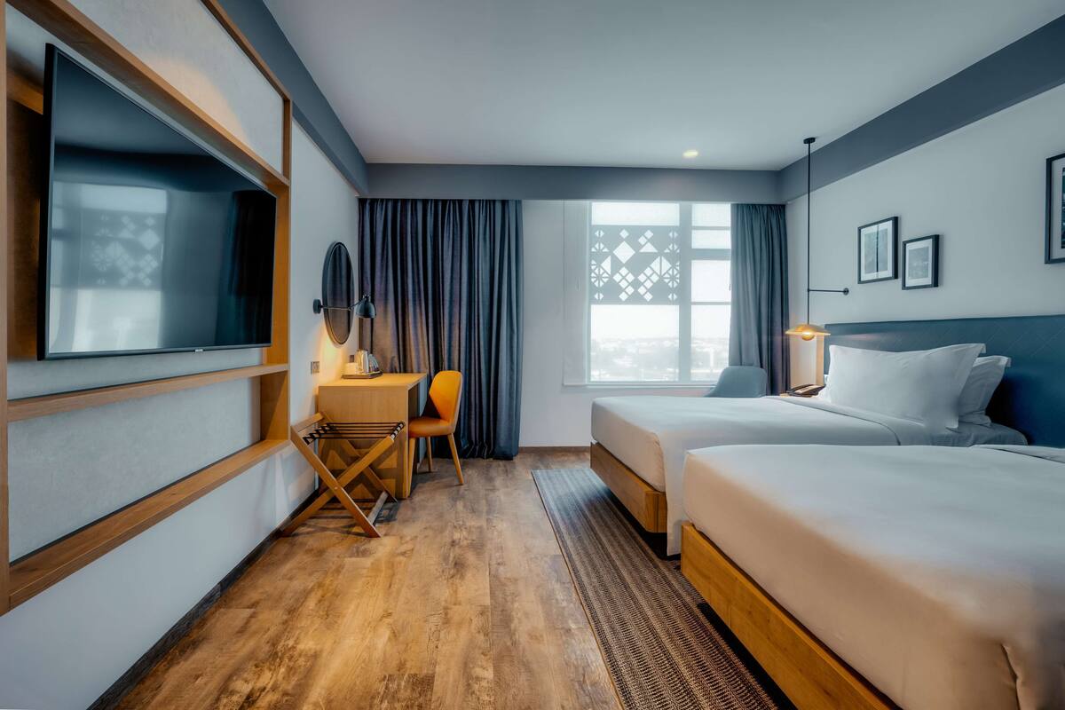 A hotel room with a bed, a desk, a chair, a TV, and a window with curtains.