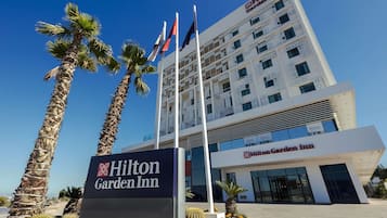 The Hilton Garden Inn building with a signboard, palm trees, and flags.