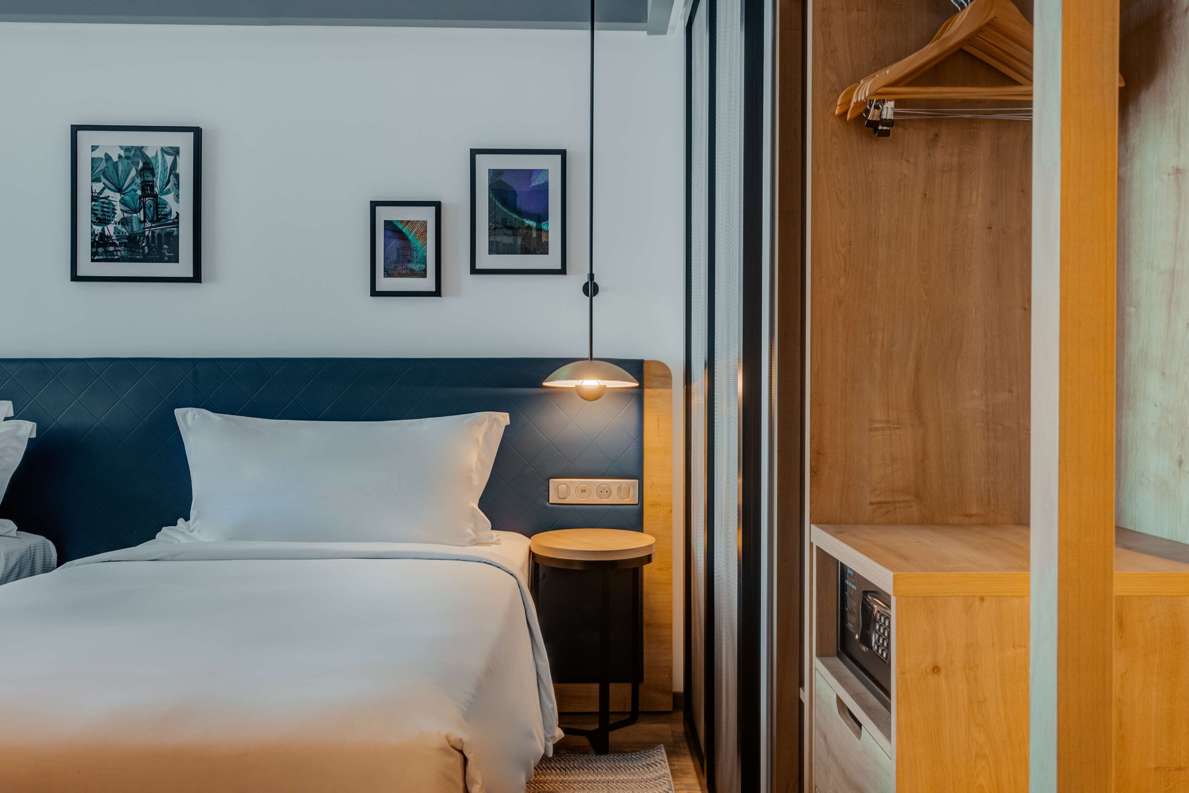 Habitación de hotel con cama, mesita de noche, lámpara y cuadros en la pared.