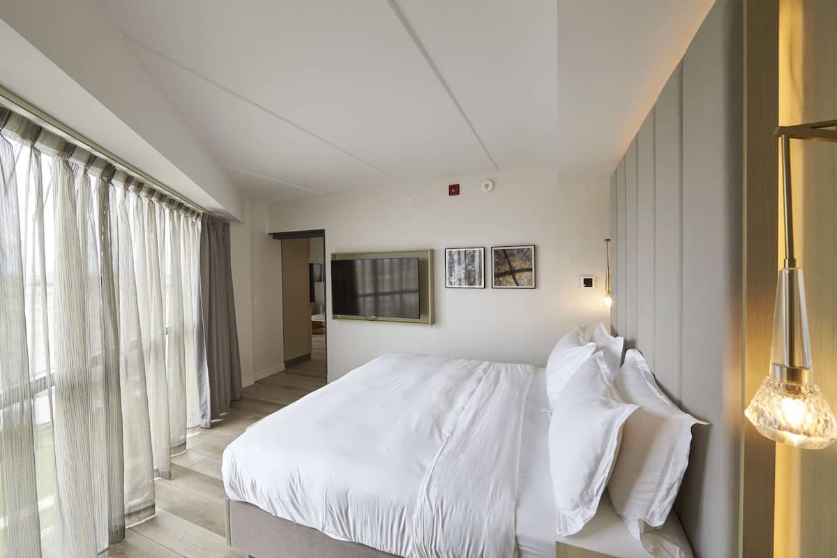 Una camera d'hotel moderna con un grande letto, una televisione a schermo piatto e un'ampia finestra con tende.