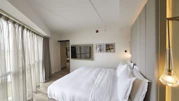 A modern hotel room with a large bed, a flat-screen TV, and a large window with curtains.