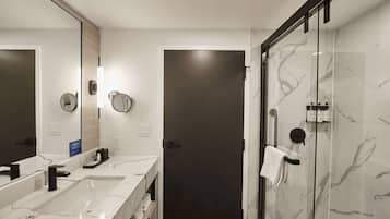 A modern bathroom with two sinks, a large mirror, and a glass-enclosed shower area.