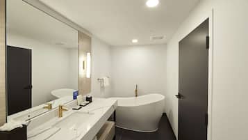 A modern bathroom with a large mirror, two sinks, a freestanding bathtub, and a dark door.