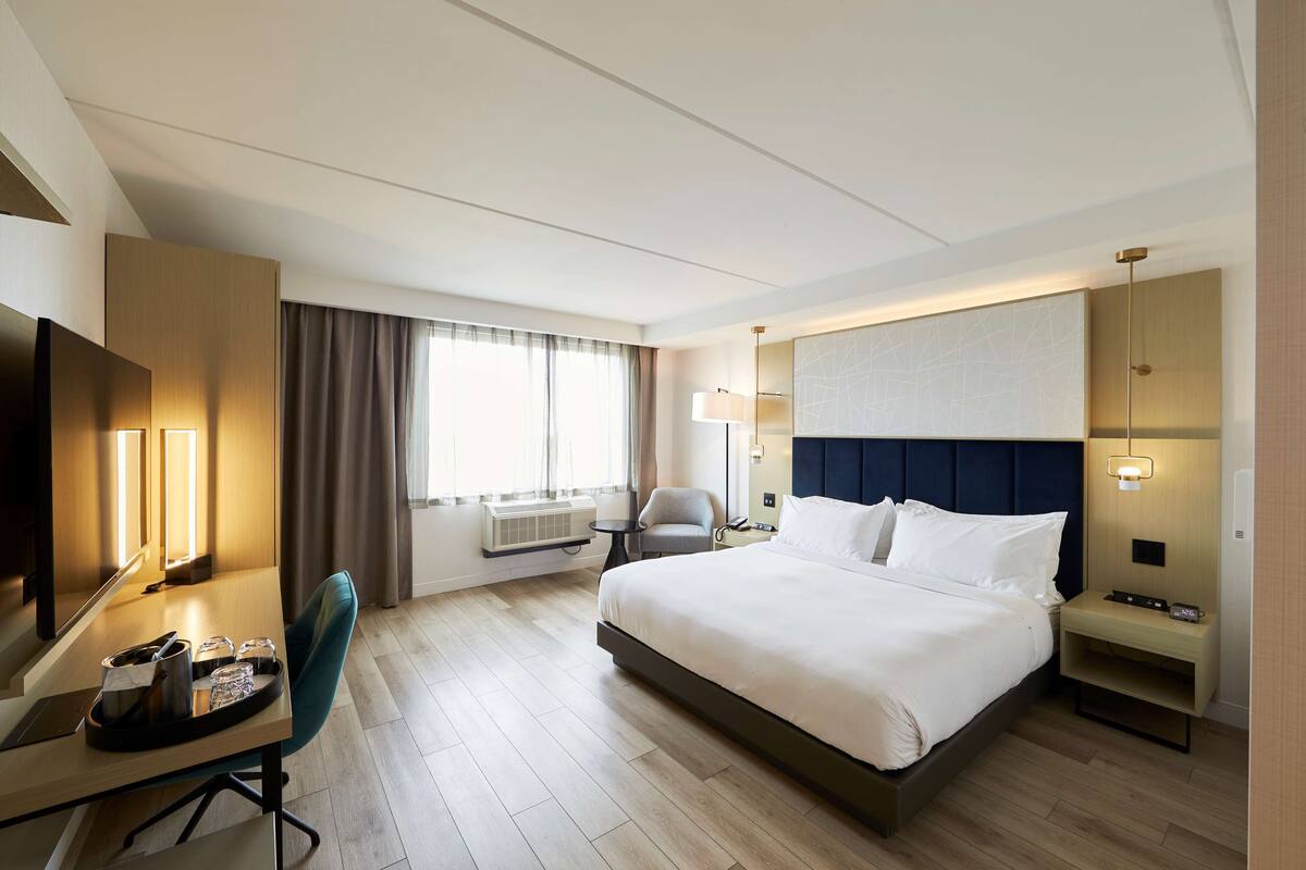 Una camera d'albergo con un letto grande, una scrivania con una sedia, una televisione e una finestra con tende.