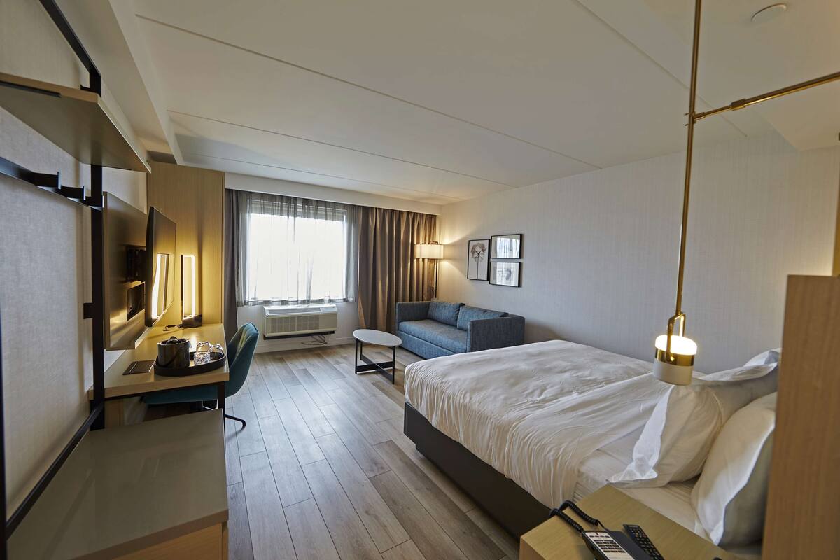 Una camera d'albergo con un letto, una scrivania con una lampada, un divano e una televisione.