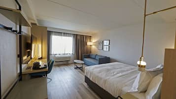 A hotel room with a bed, a desk with a lamp, a sofa, and a TV.