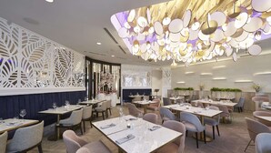 Un interior de restaurante moderno con mesas de mármol blanco, asientos cómodos, paneles decorativos en las paredes y una lámpara de techo única.
