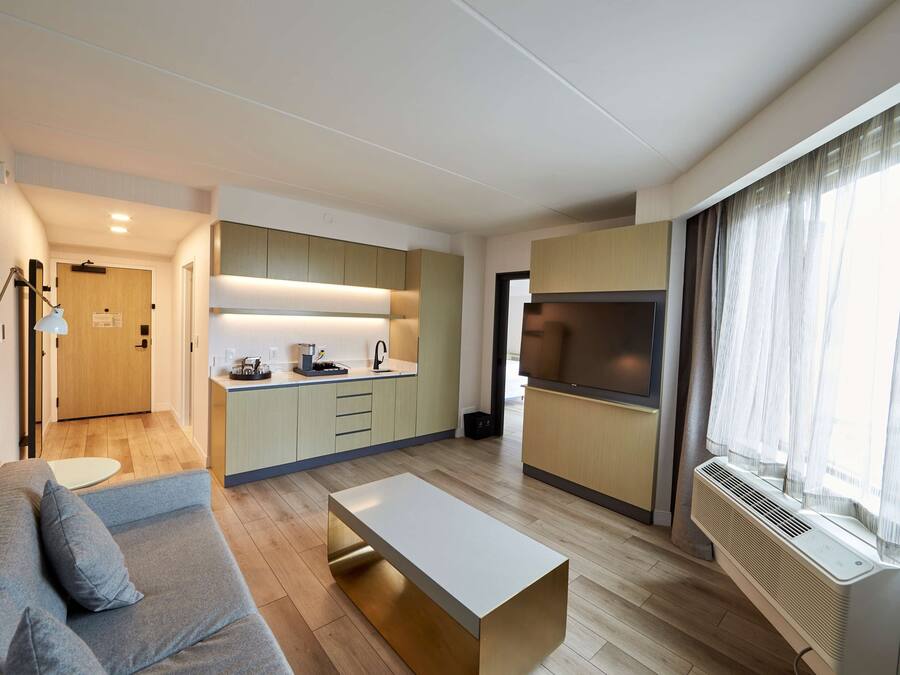Un salon moderne comprenant un canapé, une table basse et un coin cuisine avec des placards et un téléviseur.