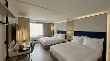 Habitación de hotel con dos camas, un escritorio con silla, televisión y un ventanal con cortinas.