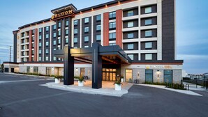 Un hotel de varios pisos con fachada moderna, que presenta una entrada destacada con un vestíbulo cubierto y plantas en macetas.