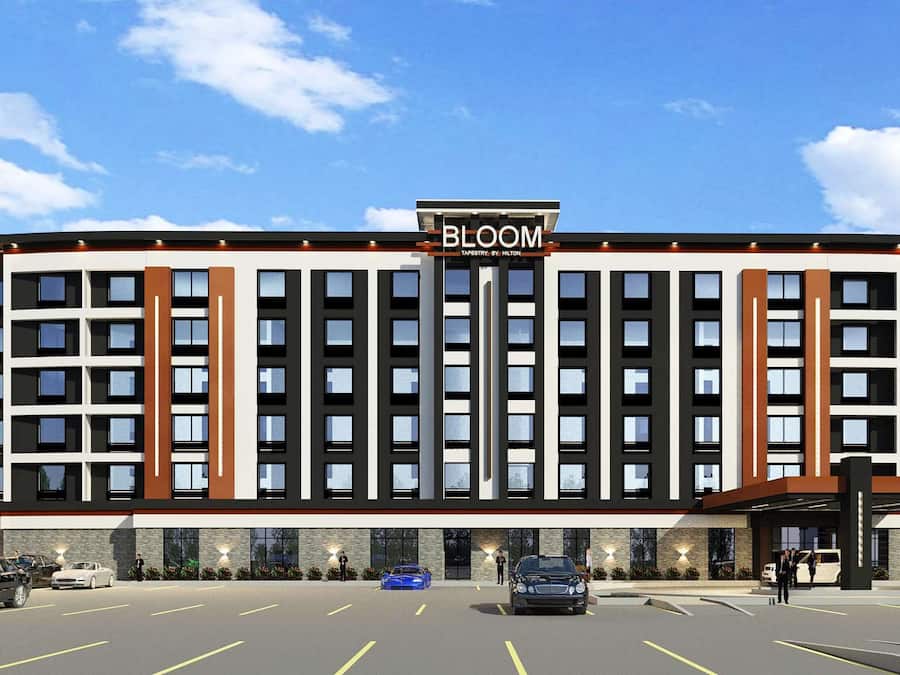 A modern hotel with a prominent 'BLOOM' sign, multiple floors, and a parking lot with several cars.