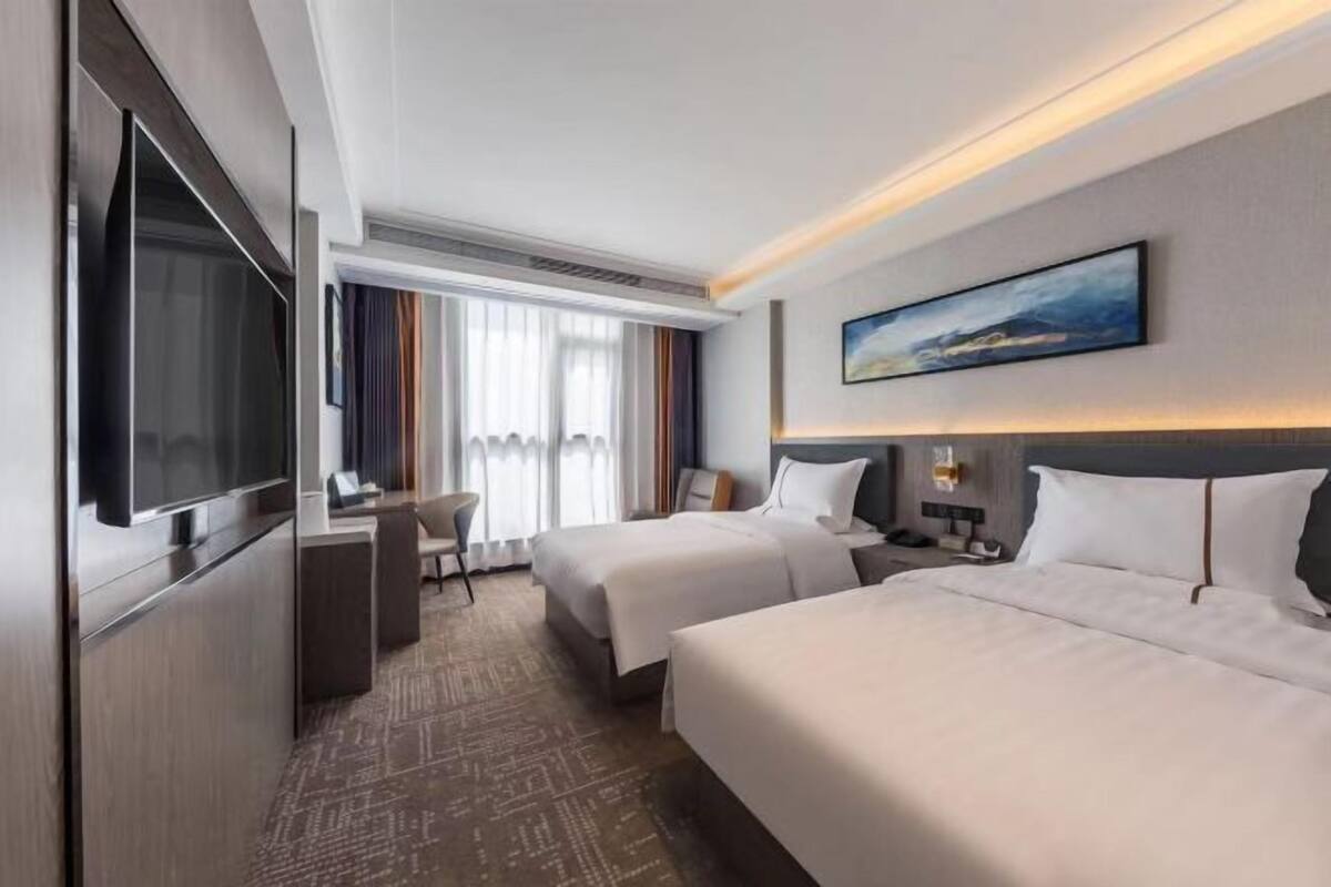 A hotel room with two beds, a desk, a TV, and a painting on the wall.