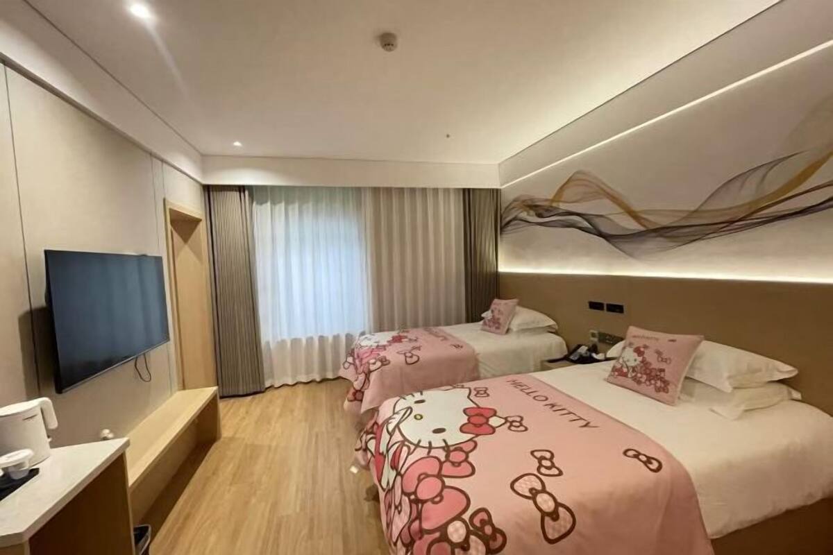 A hotel room with two beds, a flat-screen TV, a desk, and a window with curtains.